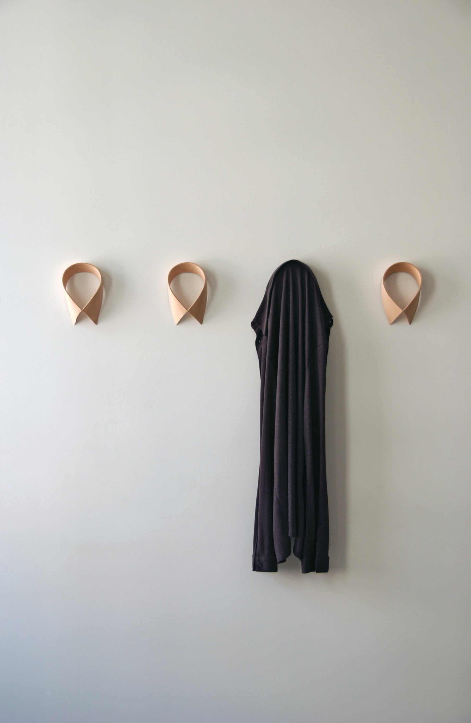Three wall hooks on a light green wall with a black coat hanging from one of them.