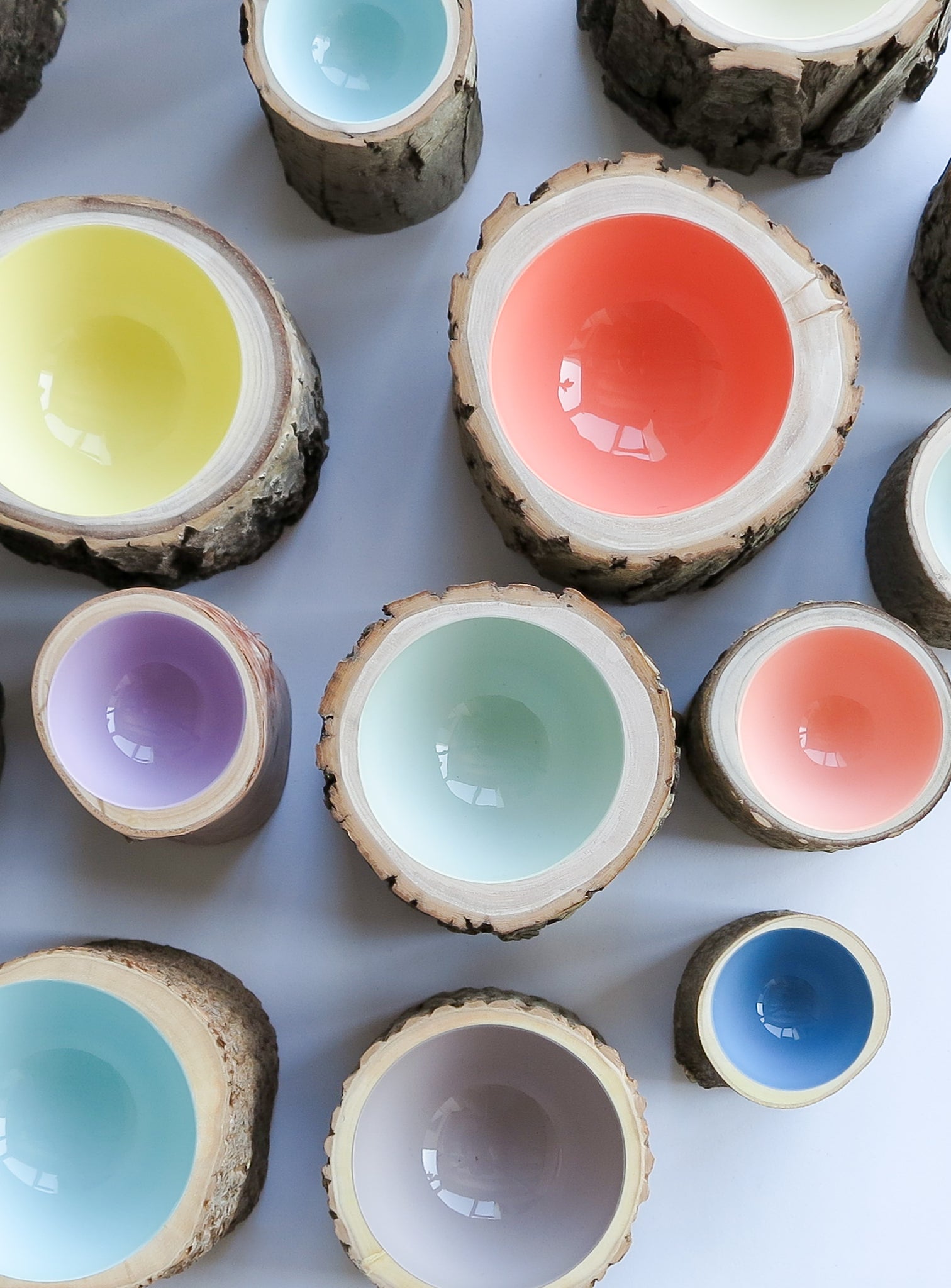 top view of group of pastel wooden Log Bowls with glossy interiors in coral, mint, light blue, light green, light yellow, and lilac purple.