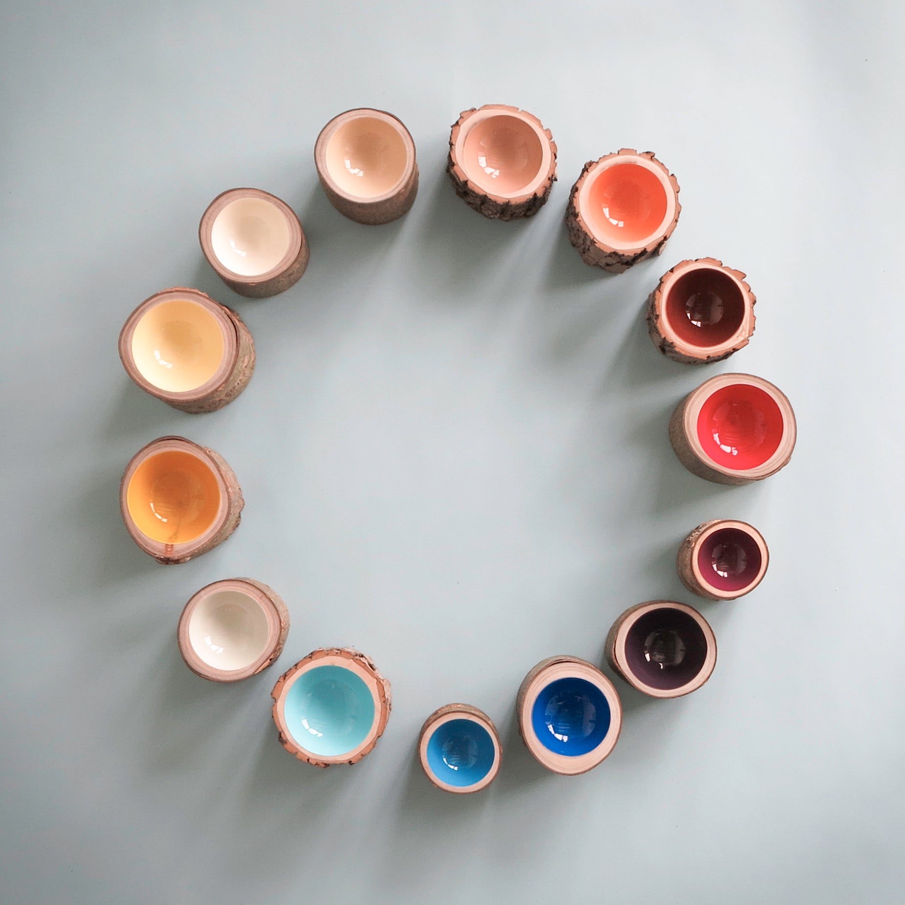 Top view of 14 wood Log Bowls in varying bright and mellow colours by Loyal Loot, arranged in a circle.